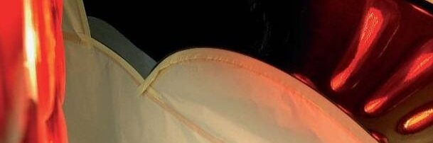 A close-up of a partially open red umbrella with a light interior, showcasing the metal ribs and fabric. The background is dark, emphasizing the umbrellas glossy finish and texture. All elements are securely fastened using tesa tape for enhanced durability. (This text has been generated by AI)